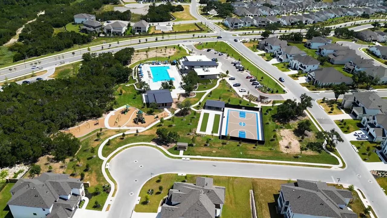 Aerial view of suburban roads, park, swimming pool and basketball court showing a spread-out neighborhood layout