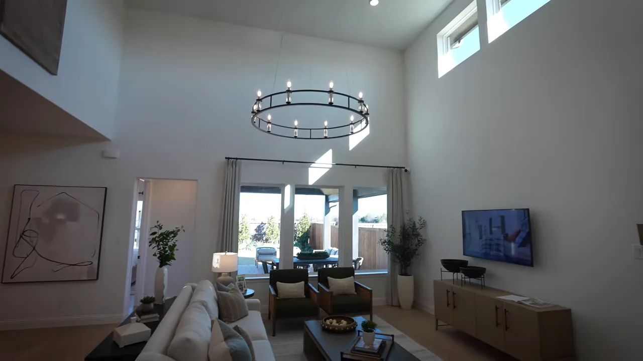 Two‑story living room with round chandelier, high ceilings, clerestory windows and a clear view to the backyard patio.
