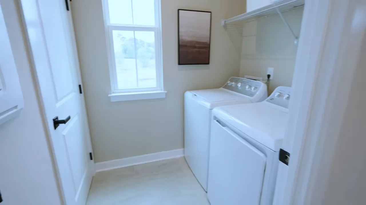 Bright laundry room with stacked washer and dryer, white cabinetry, and a window in a new construction home
