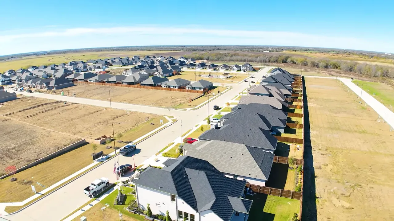 Aerial drone photo of a new-construction neighborhood with rows of houses, driveways, and vacant lots