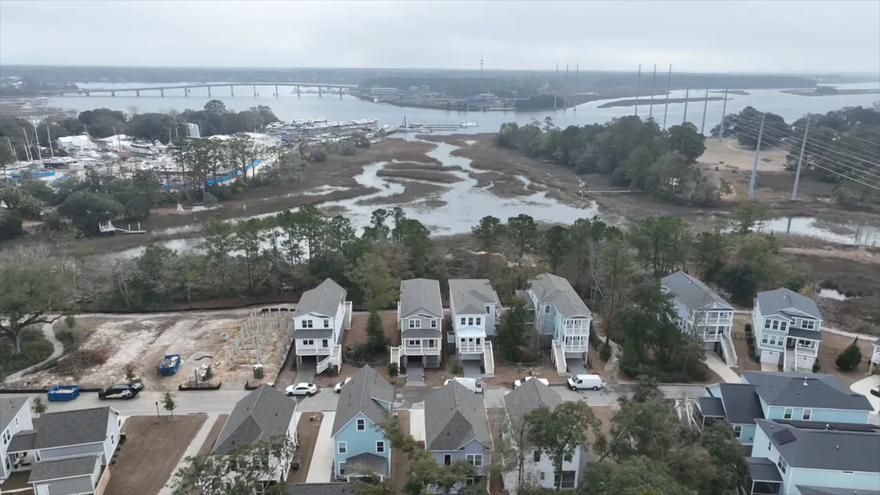 High-resolution aerial photo of suburban homes adjacent to a tidal marsh and creek, showing yards, vacant lots, and nearby water