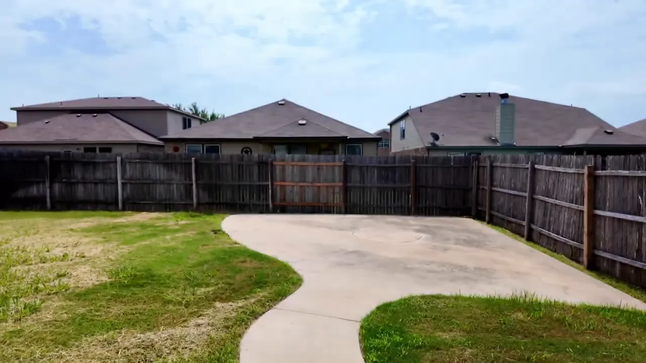 Fenced backyard with curved concrete patio and grass