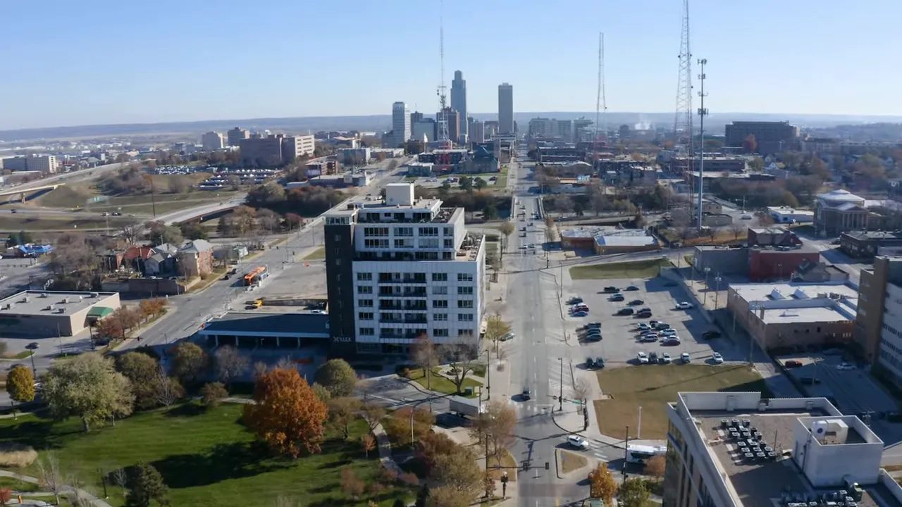 Wide aerial panorama of Omaha showing midtown buildings, streets, parking lots and the downtown skyline in the distance.