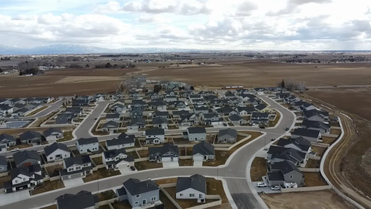 High‑resolution aerial photo of a new suburban neighborhood bordered by farmland under a cloudy sky