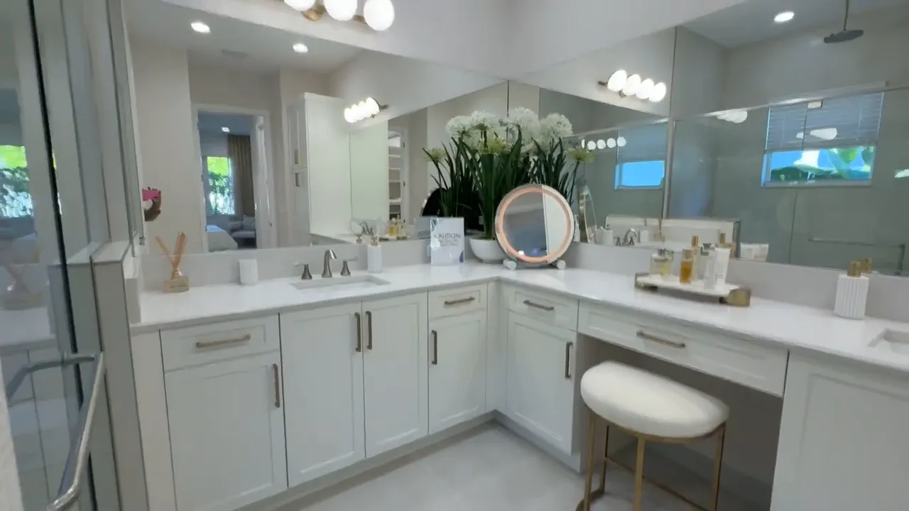 Primary bathroom with dual vanity, large mirrors, makeup seat, and glass shower
