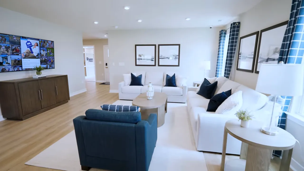 Open living room with two white sofas blue chair wall mounted television and recessed lighting
