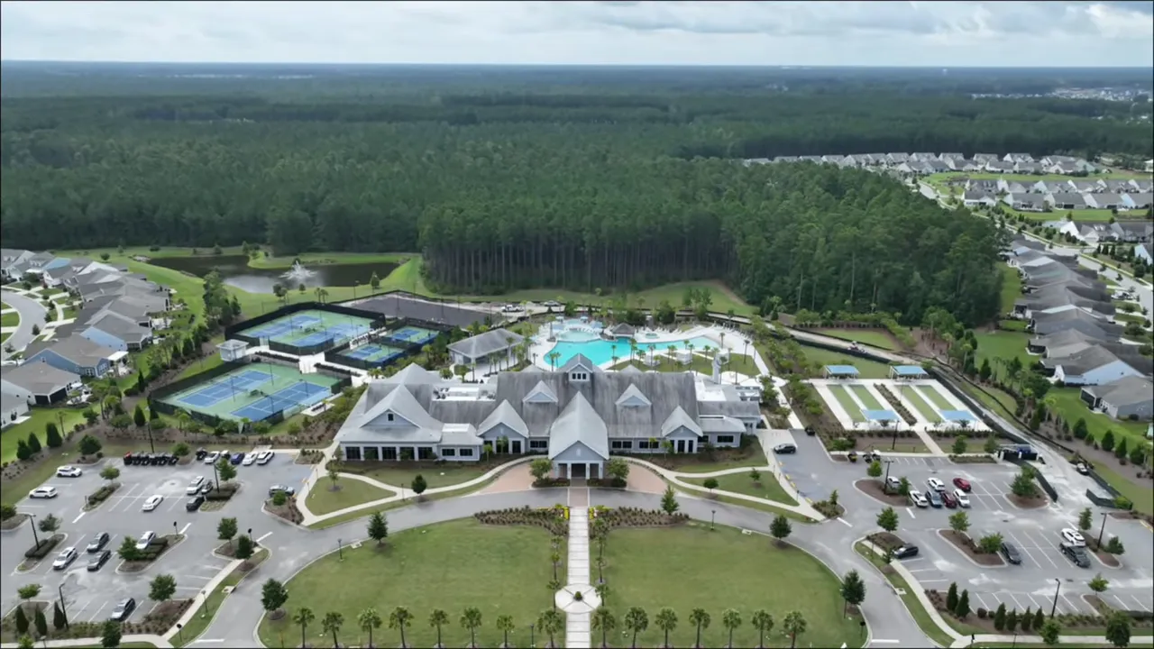 Aerial drone view showing Del Webb Nexton clubhouse, lagoon-style pool, pickleball/tennis courts and surrounding homes in Summerville, SC.