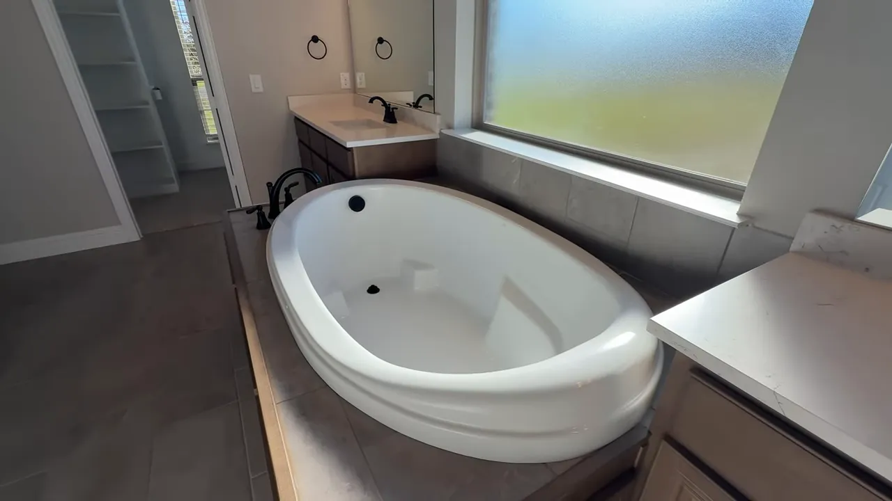 Large oval soaking tub in primary bathroom with window and vanity