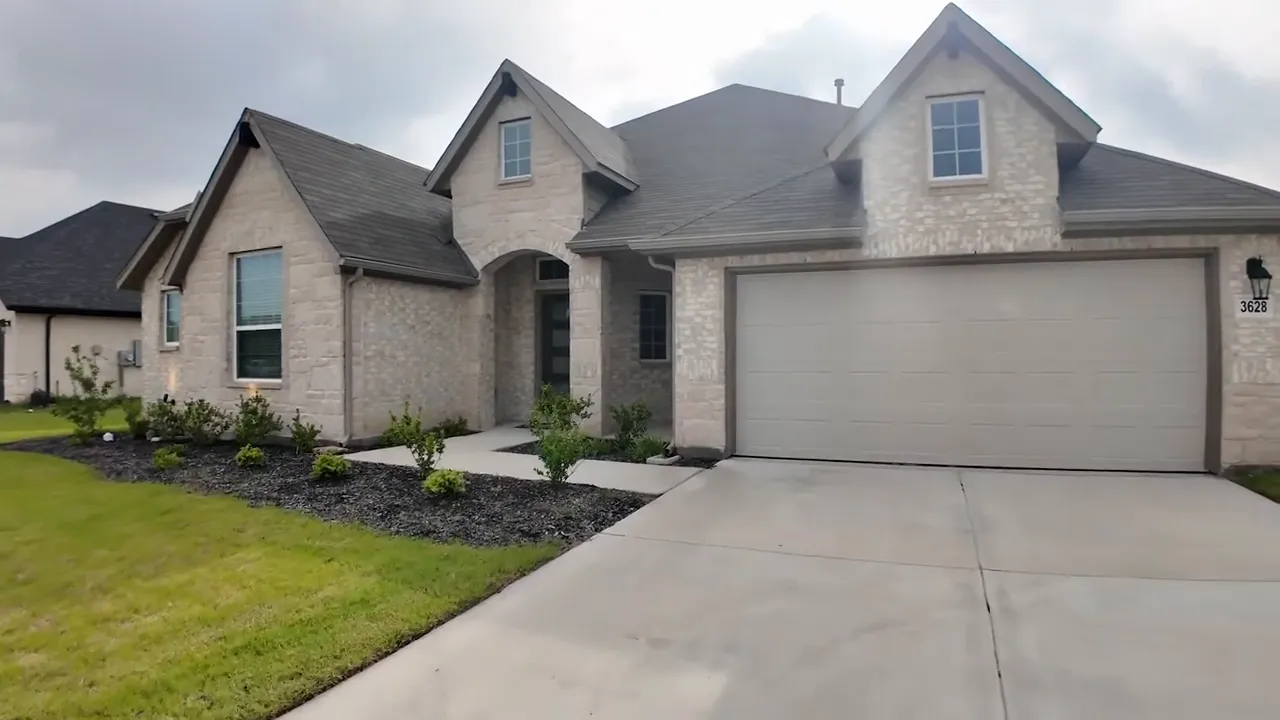 Front exterior of a light brick house with a wide driveway and two car garage