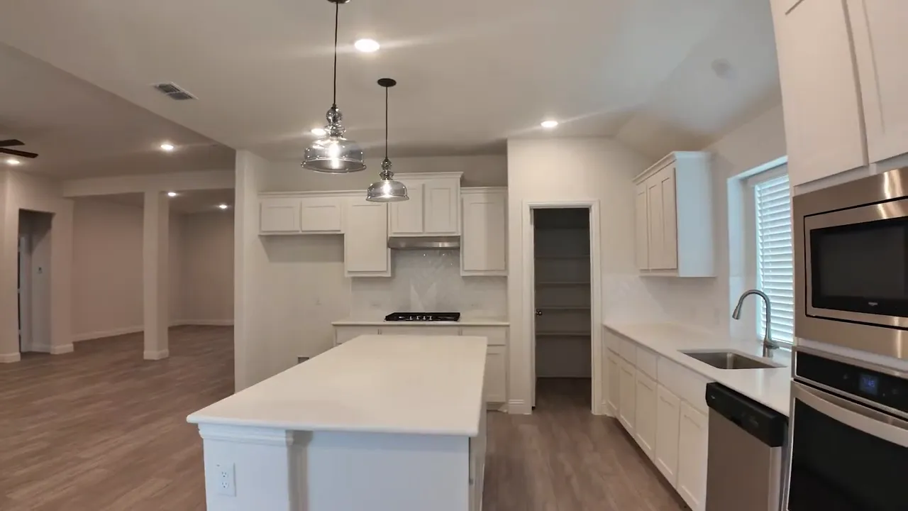 White kitchen with large island pendant lights double ovens and open living area