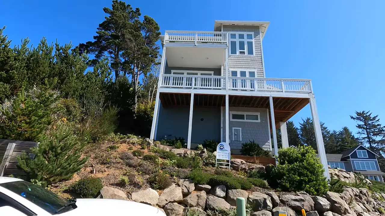 Tall coastal home on a landscaped hillside with covered decks