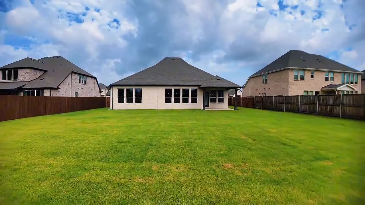 View from backyard toward rear of house showing wide lawn and covered patio