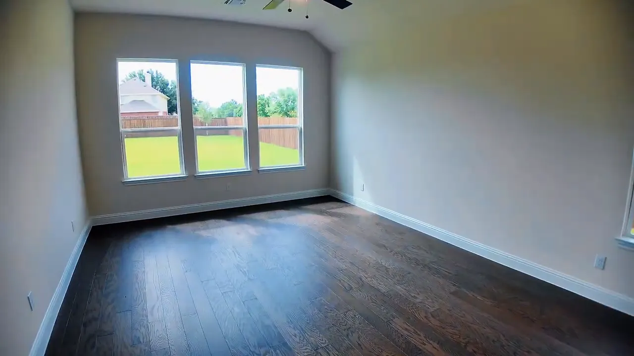 Large primary bedroom with dark wood floors and windows facing backyard