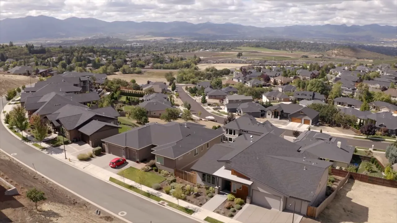 Aerial photograph of a residential subdivision with newer homes, streets, yards and rolling hills in the distance.