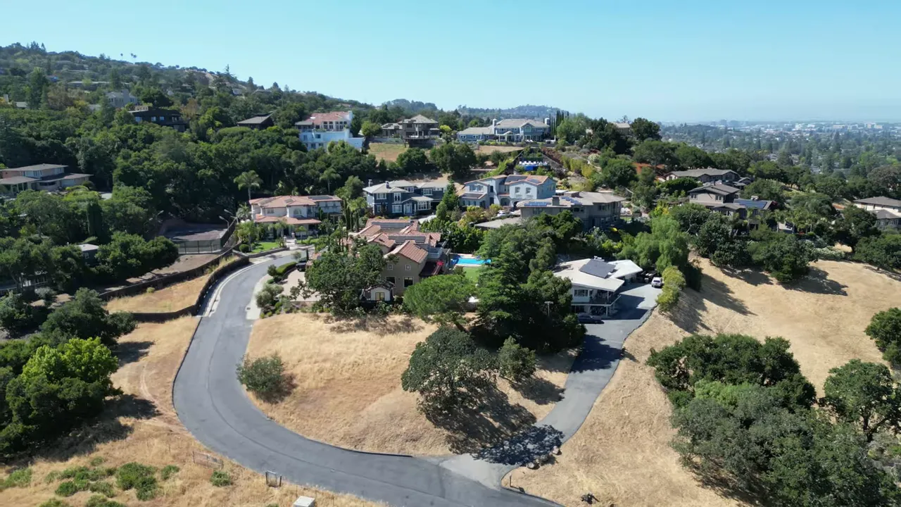 Aerial neighborhood view showing homes near open land and hillside greenery