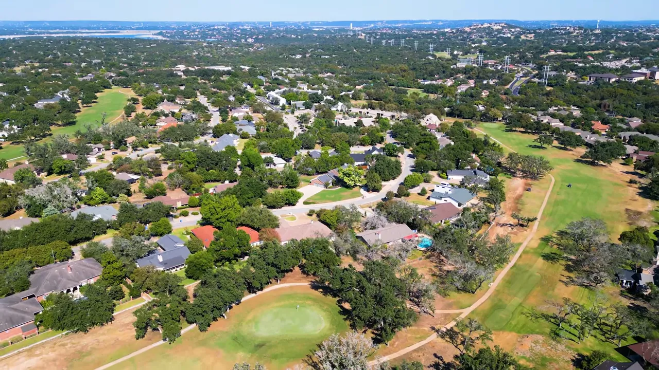 Wide aerial view of Lakeway showing neighborhoods, golf course fairways, lots of trees and Lake Travis in the distance