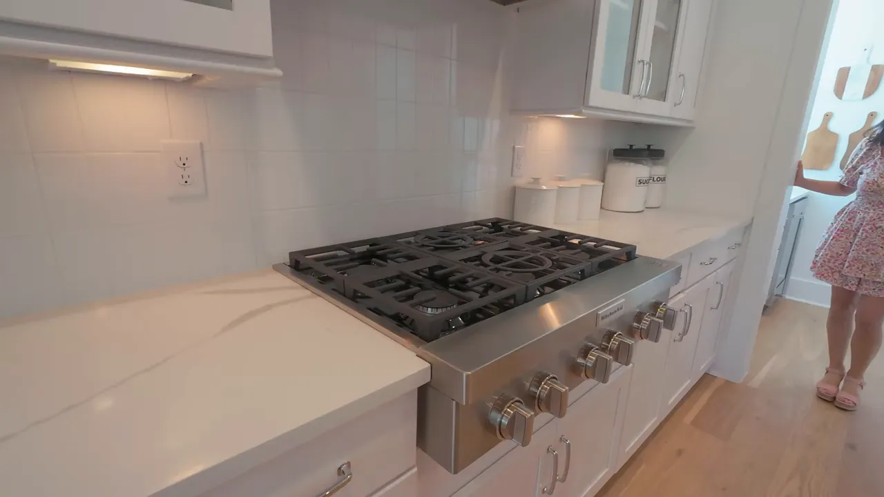 Six burner gas range beneath a white vent hood and white cabinets