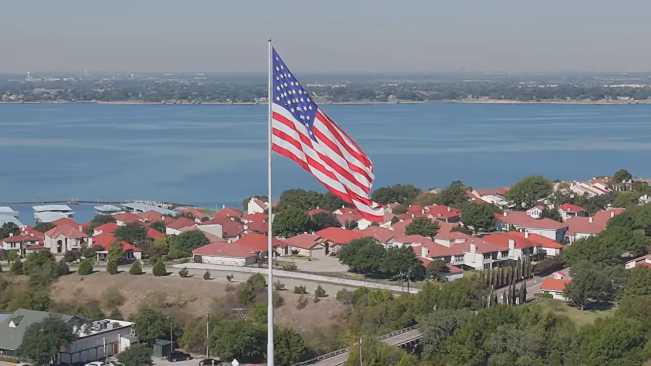 Aerial view of McLendon-Chisholm, TX homes near Rockwall with American flag and lake backdrop