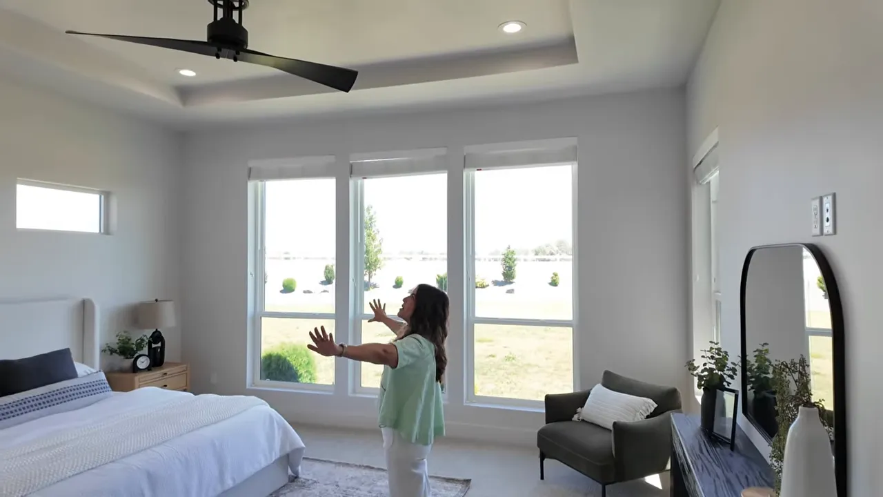 Primary bedroom with tray ceiling fan large windows and bed