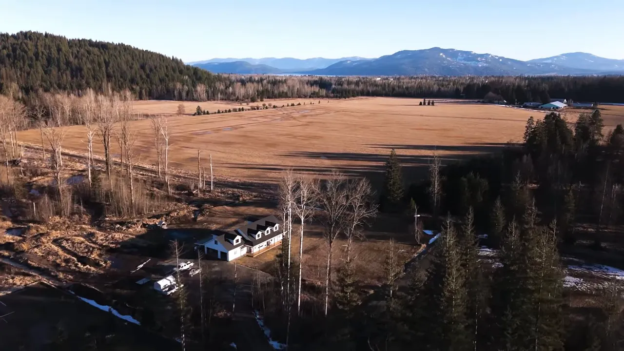 Aerial view of expansive farmland with a farmhouse, tree lines, and distant mountains.