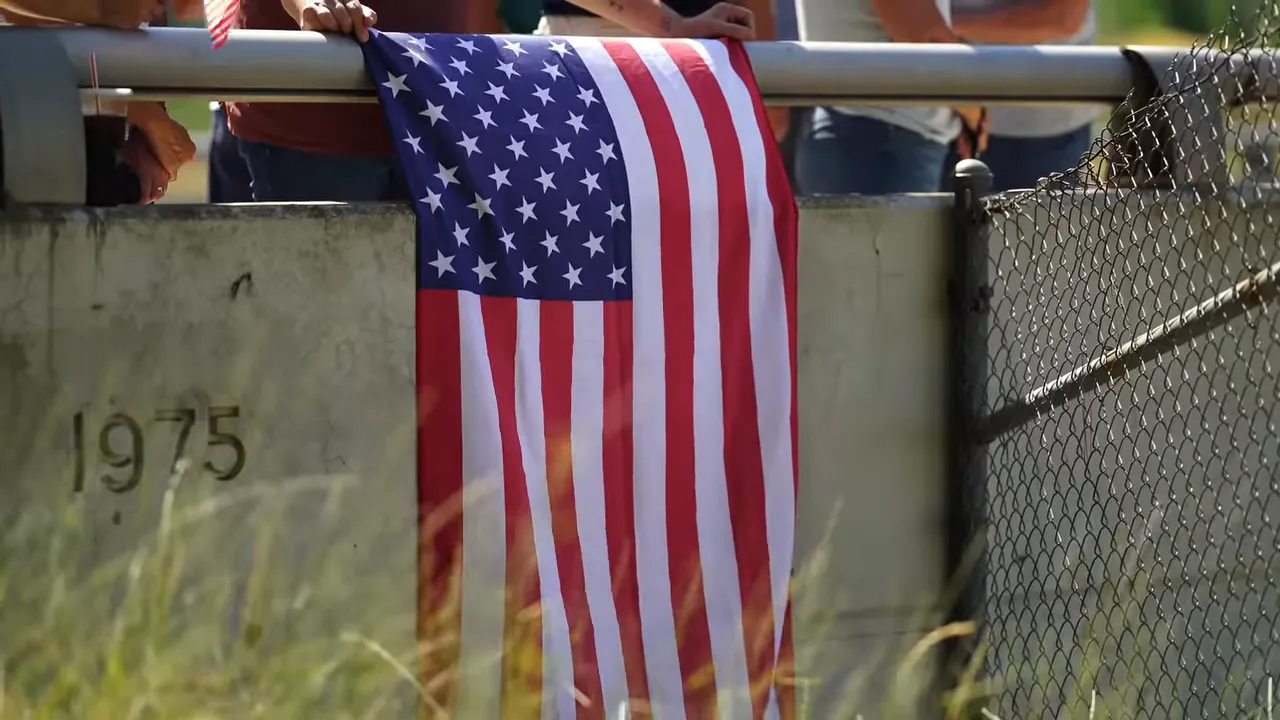 Clear view of an American flag hanging over a concrete railing with people behind it