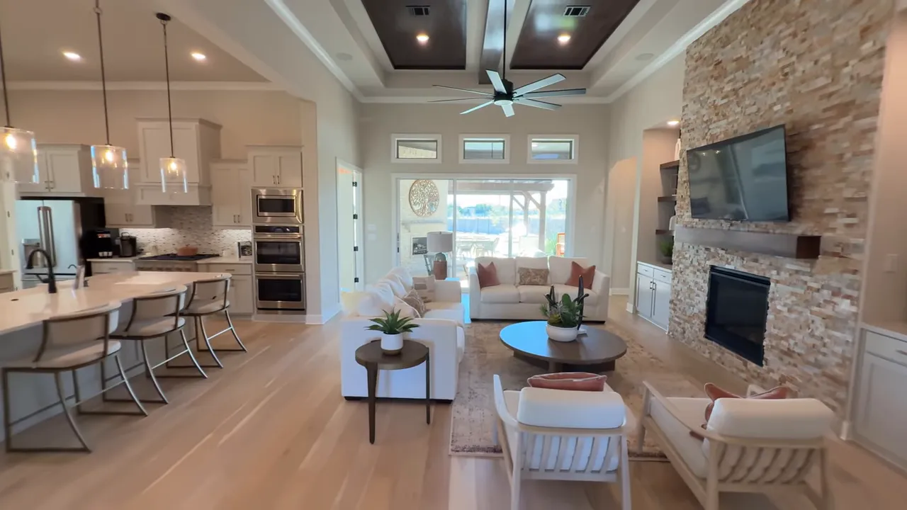 Bright open-plan living room with kitchen, seating area, stone fireplace, large windows and inset ceiling beams