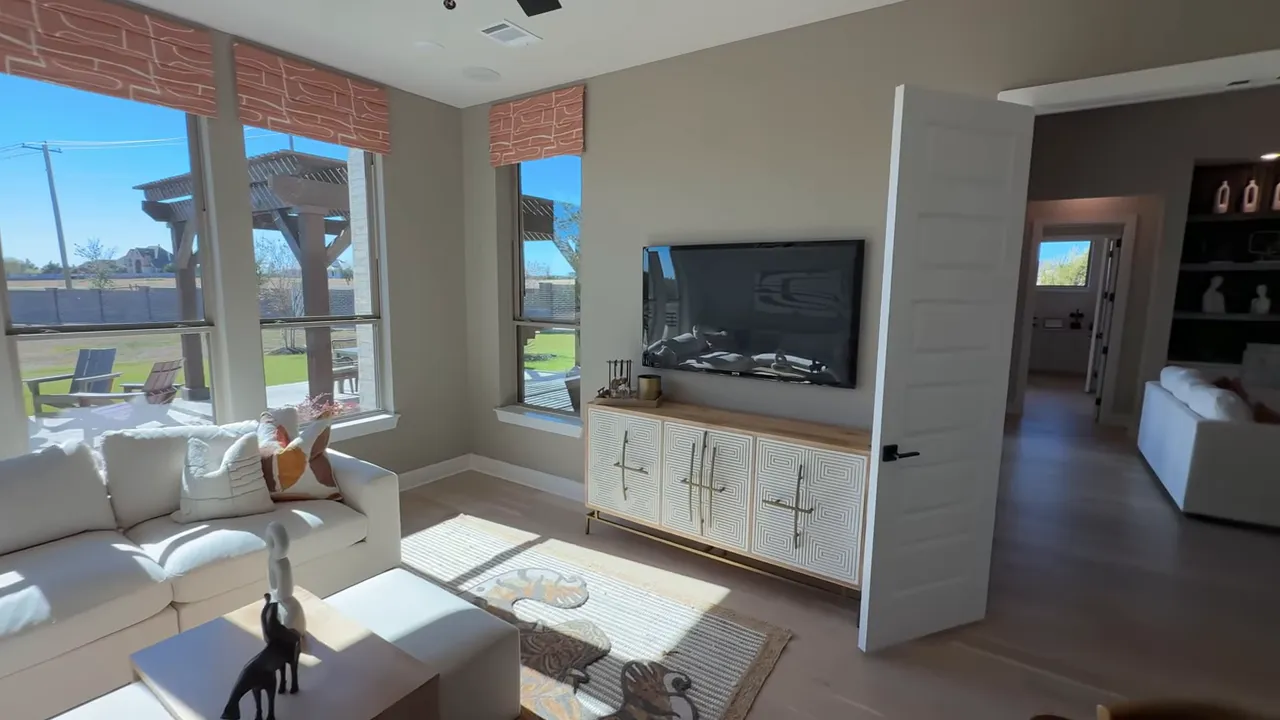 Media room showing wall-mounted TV, storage console, open privacy door and hallway access.