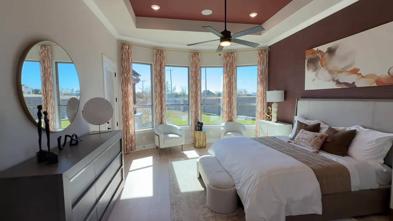 Primary bedroom with bay of tall windows, tray ceiling with accent color, bed and seating area
