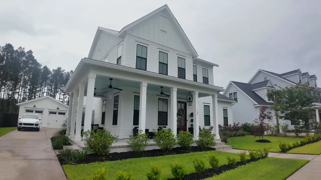 Front exterior of white two story home with wide wraparound porch and detached garage in the back