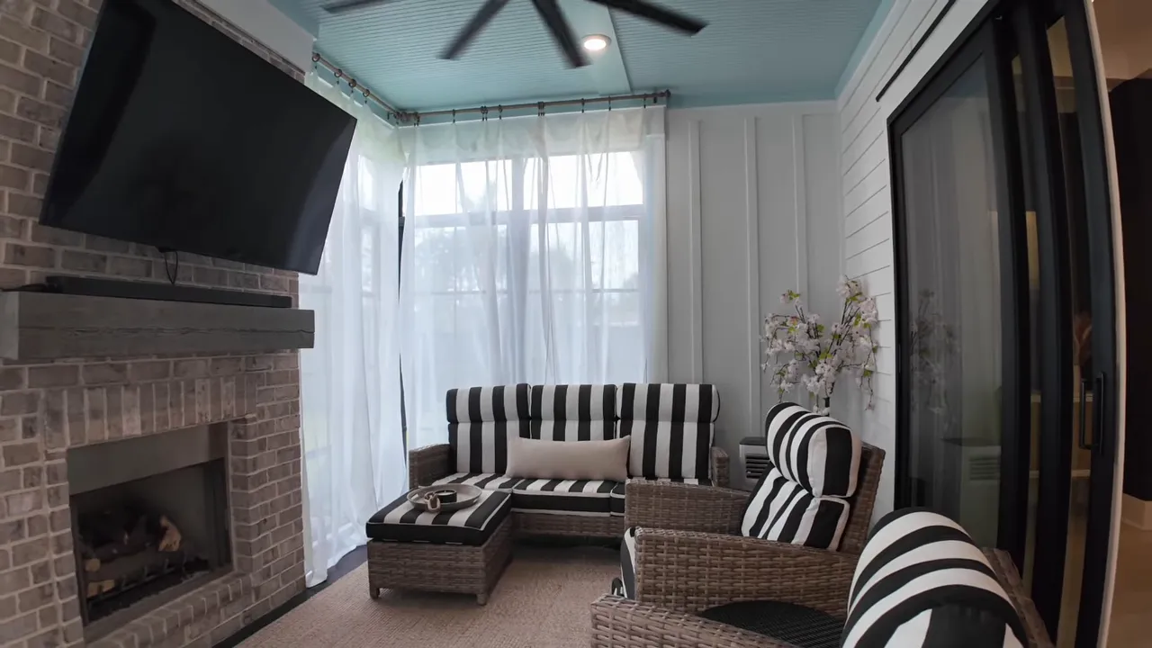 Three season room with brick fireplace, television, striped seating, and ceiling fan