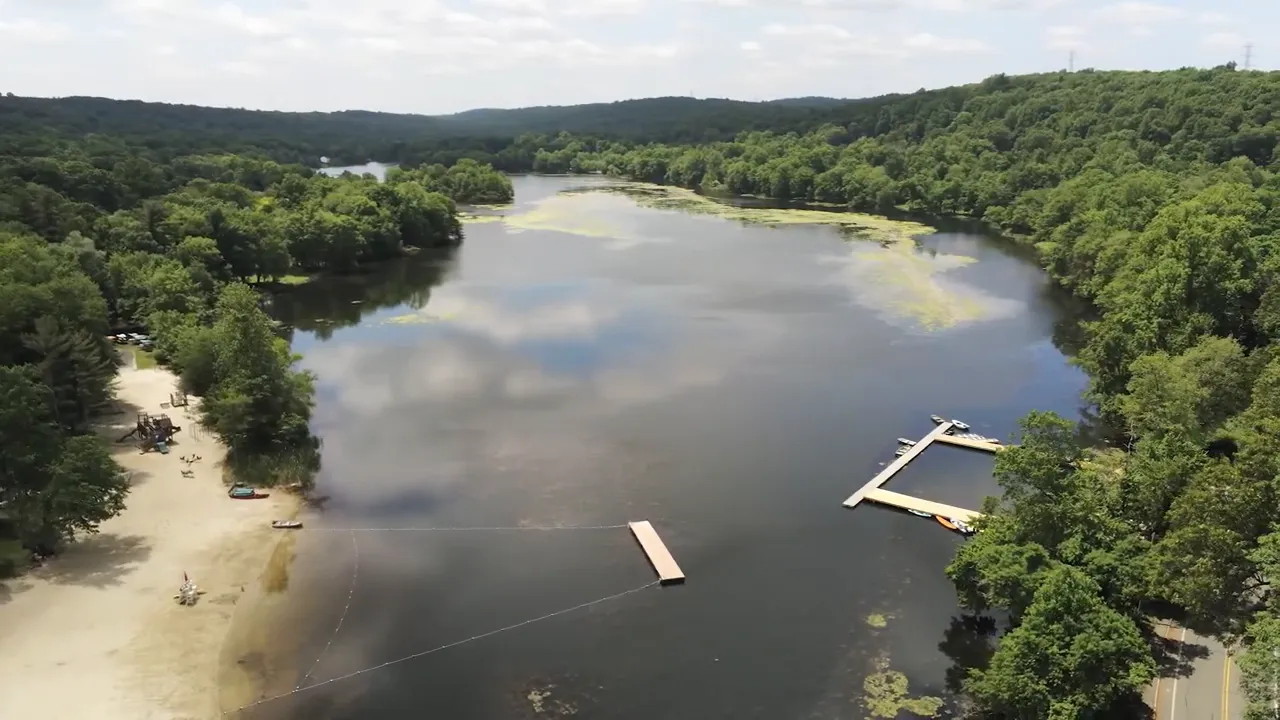 Aerial view of lake with sandy shoreline floating docks and wooded hills