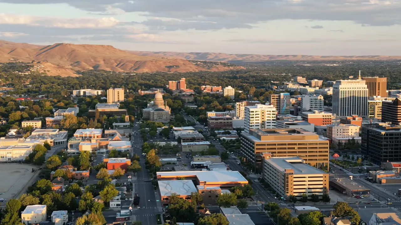 Aerial view of downtown Boise with buildings, tree-lined streets and foothills in the background