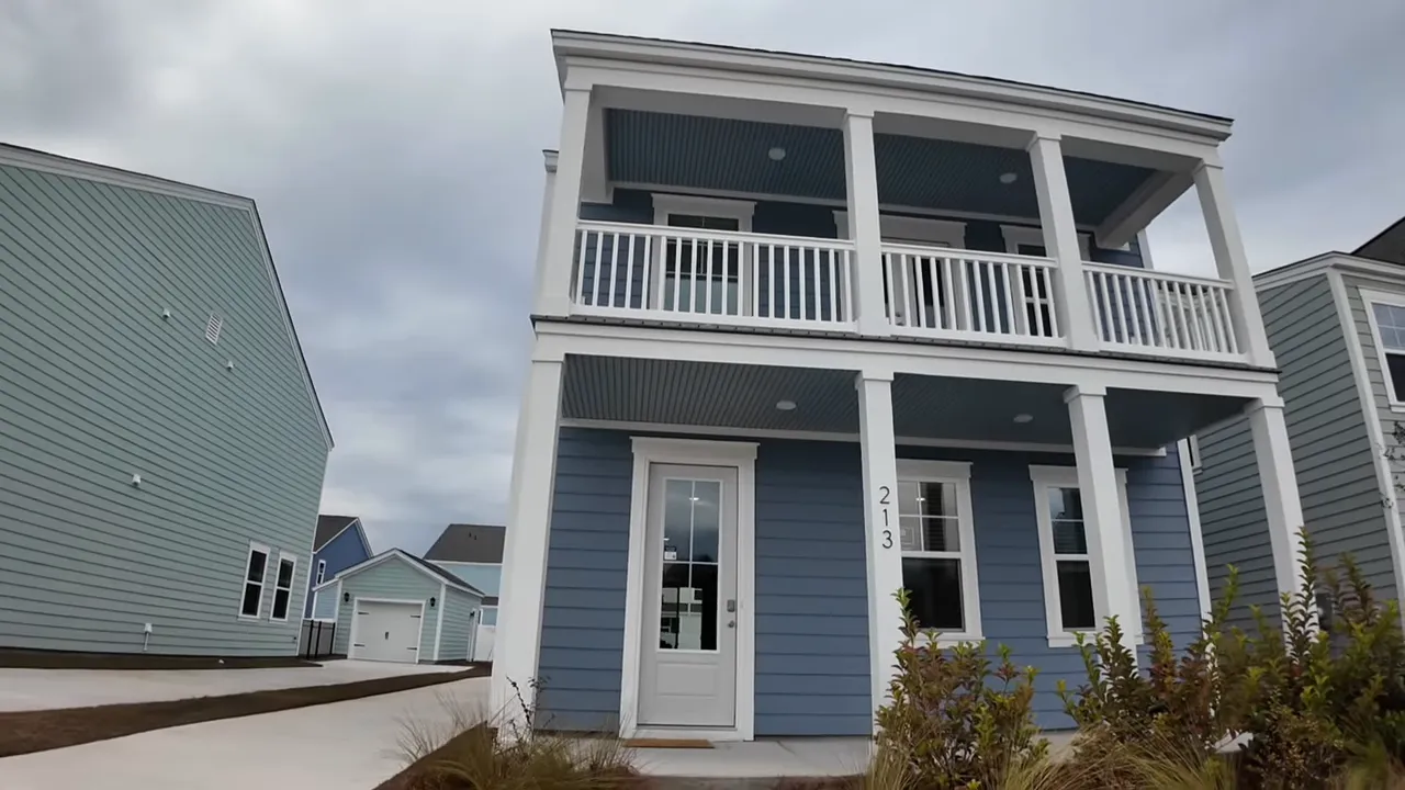 Angled exterior view of a blue two-story house with neighboring garage and driveway