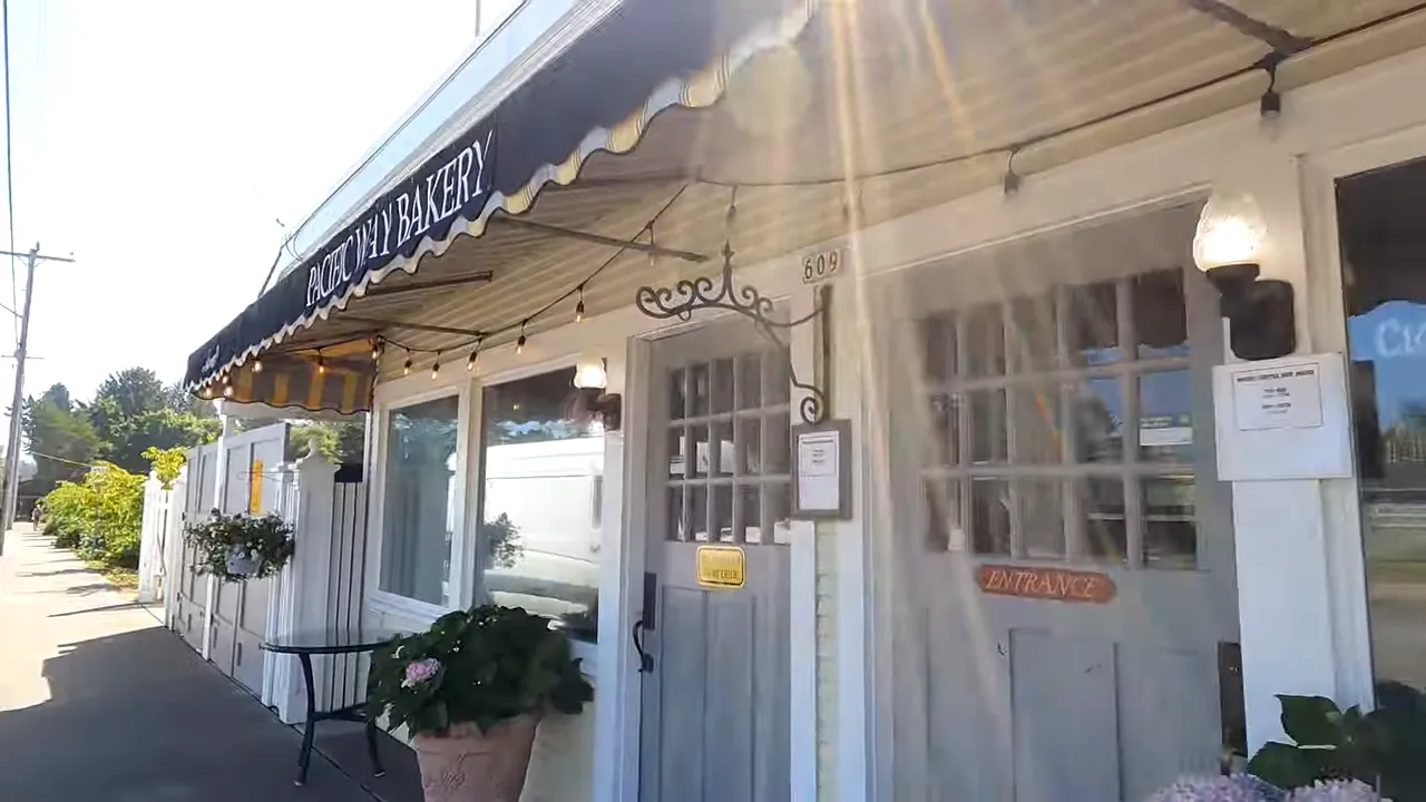 White bakery storefront with striped awning and flower planters