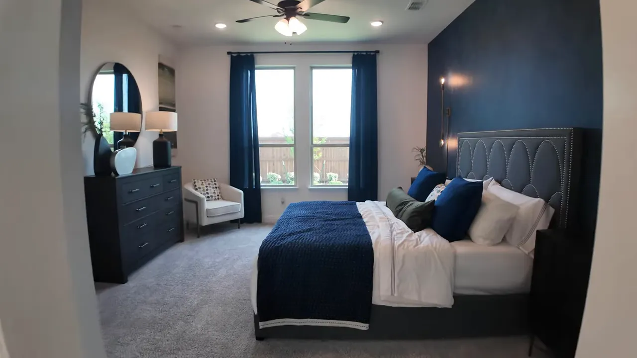 primary bedroom with blue bedding dresser chair and large windows