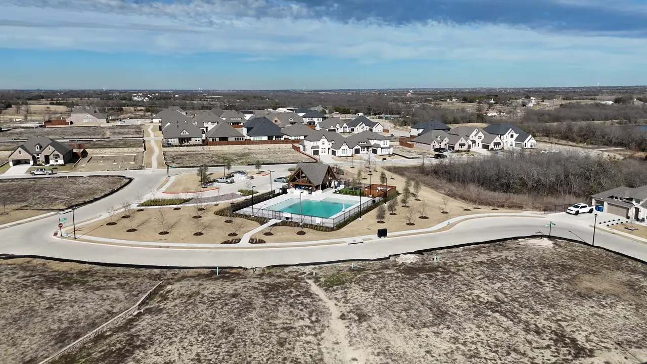 wide aerial shot of neighborhood with pool, walking paths, empty lots and surrounding homes