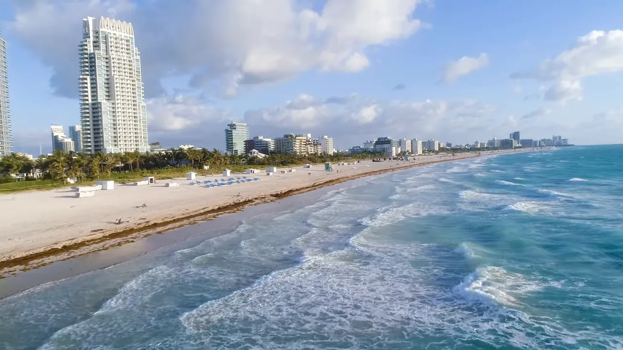 Aerial view of a Florida beach with waves, sandy shoreline and coastal buildings under blue sky