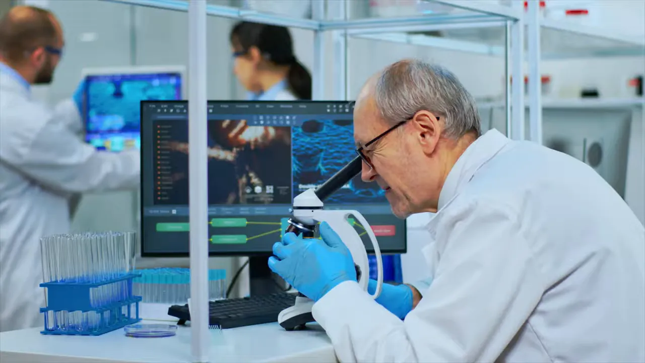 Scientists in a laboratory, a researcher looking into a microscope with monitors and test tubes visible