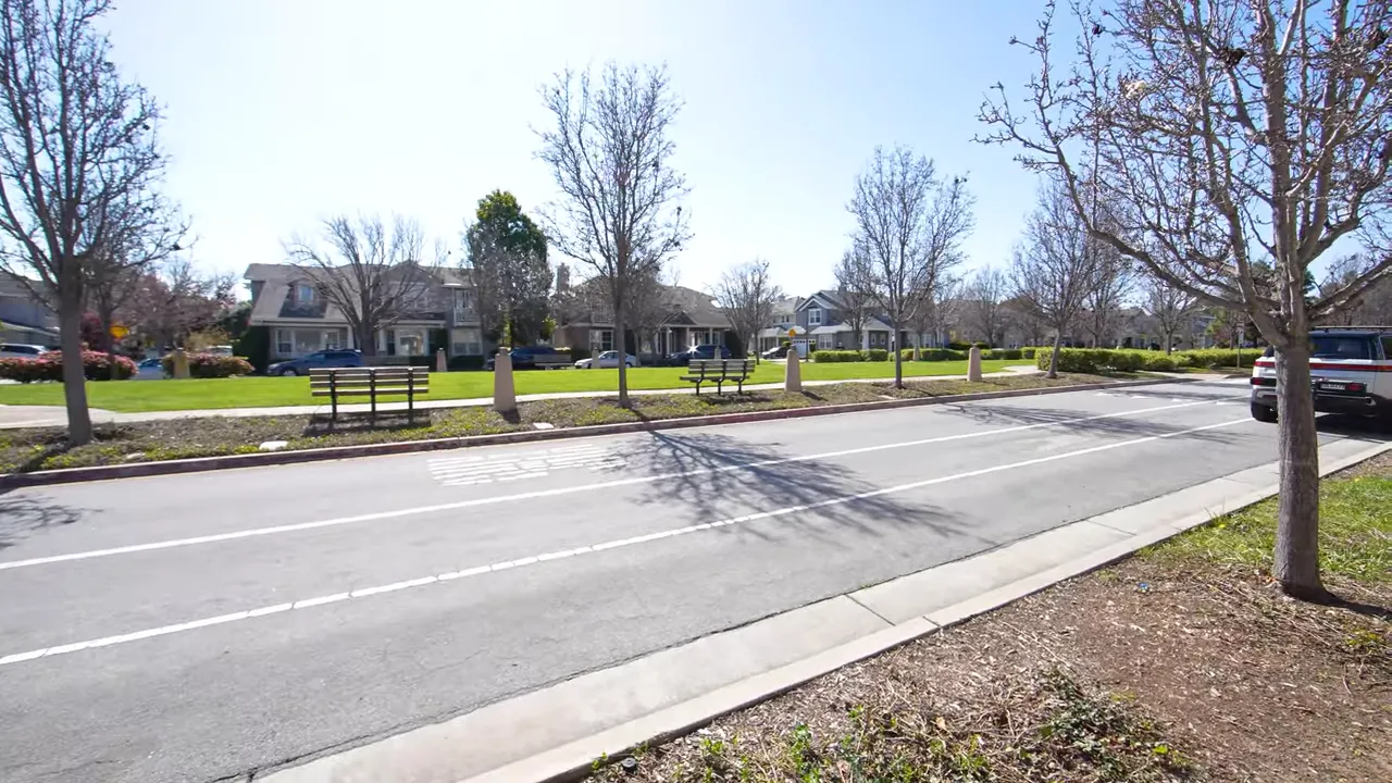 Grassy park strip with benches across the street from houses and tree-lined sidewalks