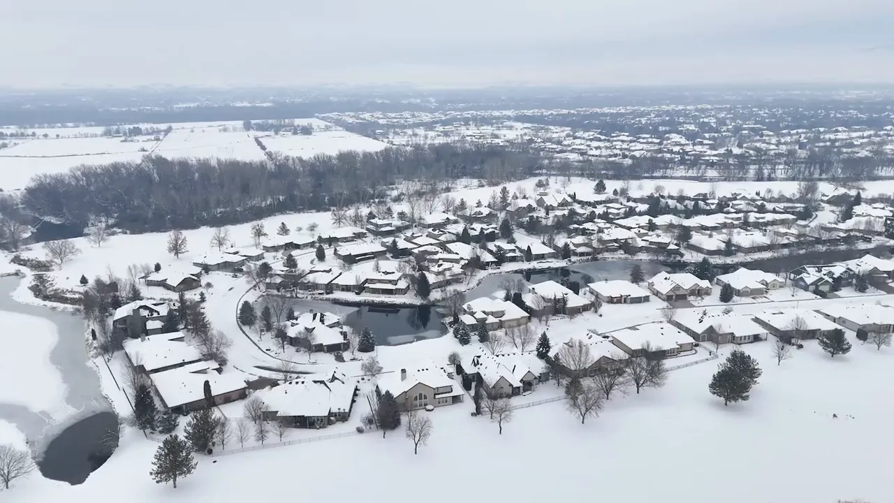 Snow covered neighborhood with winding roads homes and open white landscape