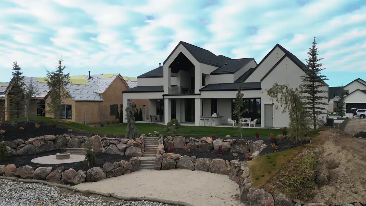 Exterior rear view of the home showing a sandy beach area, circular fire pit, terraced rock walls, lawn and a private pond