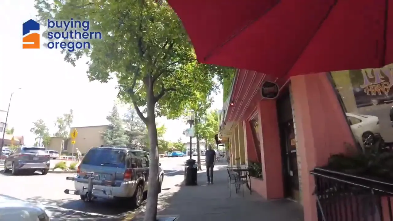 Sidewalk lined with storefronts outdoor seating and parked cars downtown