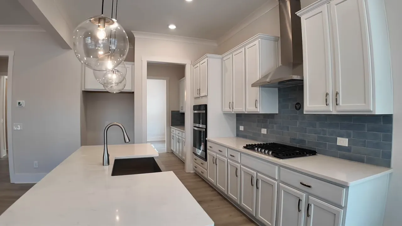 kitchen view showing white quartz island with sink, pendant lights, blue subway tile backsplash, cooktop and hood