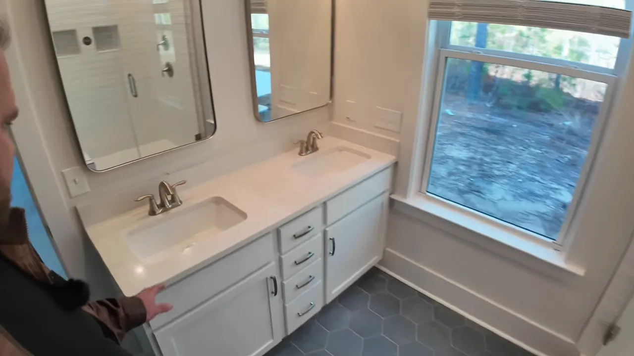 Primary bathroom double vanity, mirrors, hexagon tile floor and window overlooking yard