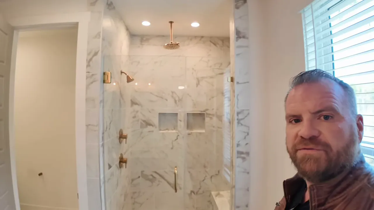Marble-tiled walk-in shower with glass door, bench and gold-toned shower fixtures