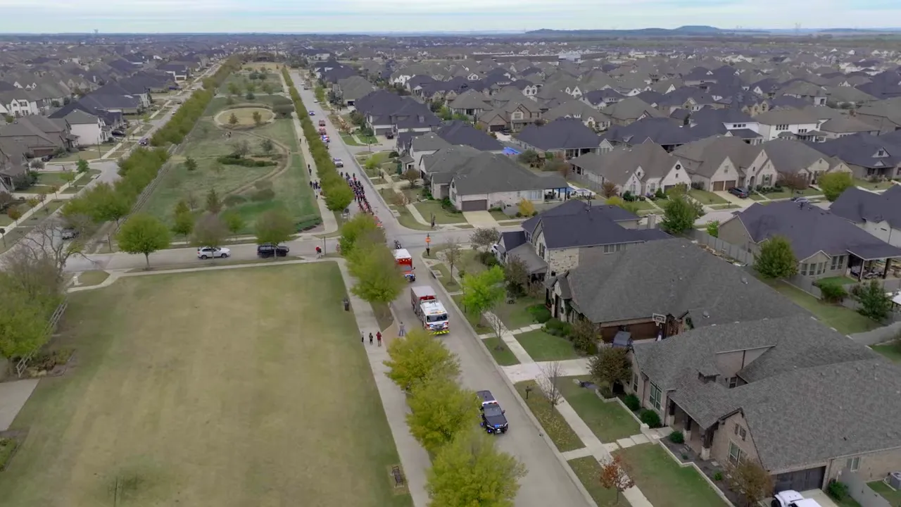 Aerial drone view of a Dallas–Fort Worth subdivision showing rows of new homes, open lots, streets, and yards.