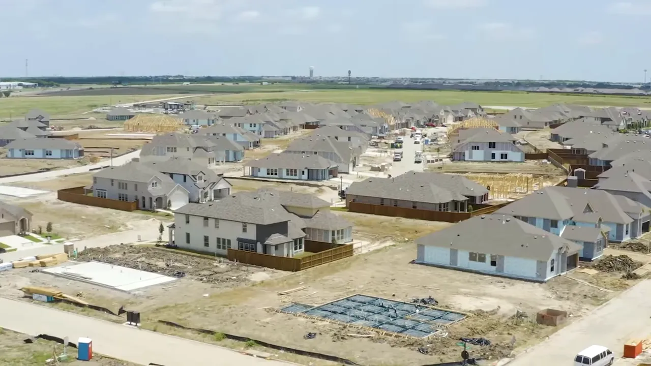 Aerial view of new-home construction showing foundation slabs, framed roofs, and houses in various stages of build in a Texas subdivision