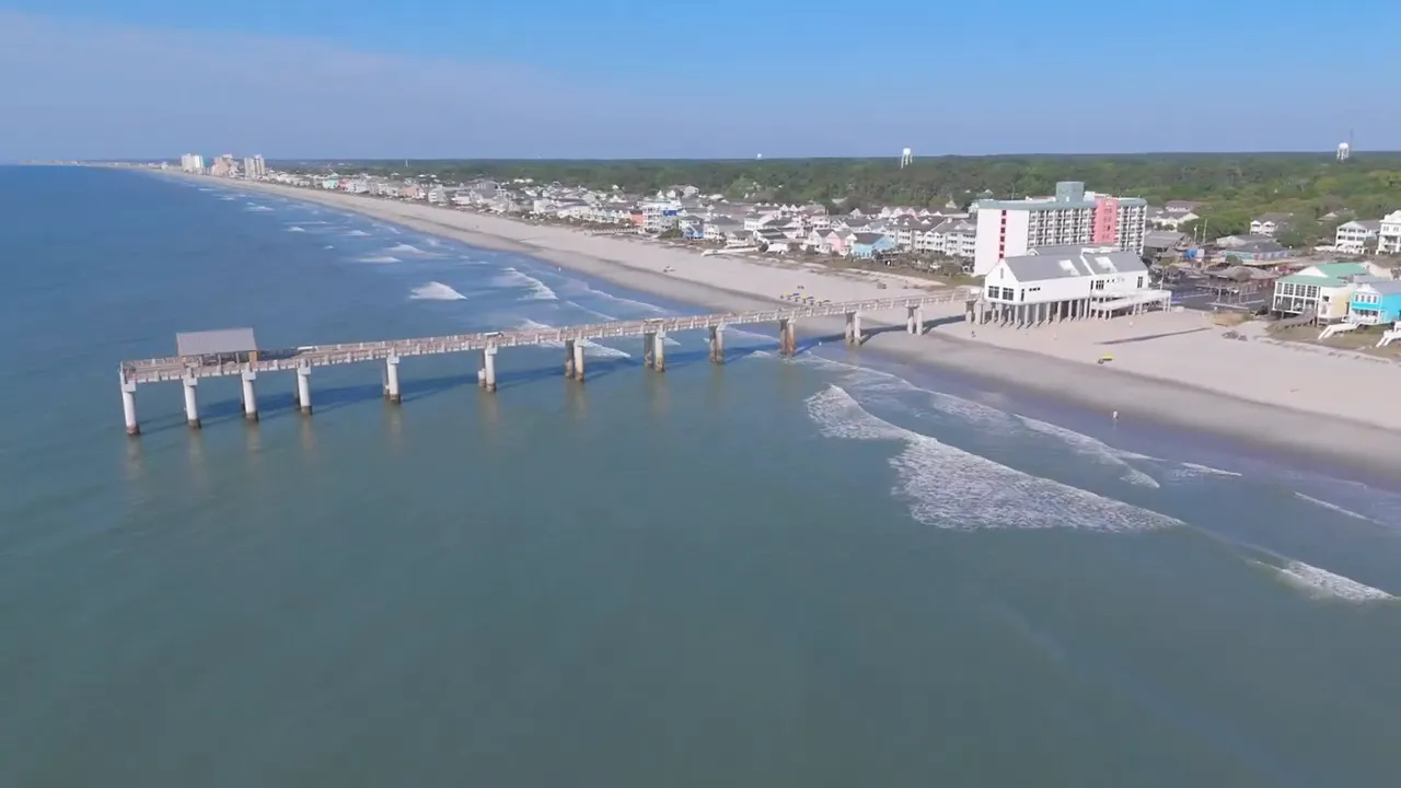 Aerial shot of Myrtle Beach coastline and pier showing a wide, lightly populated beach