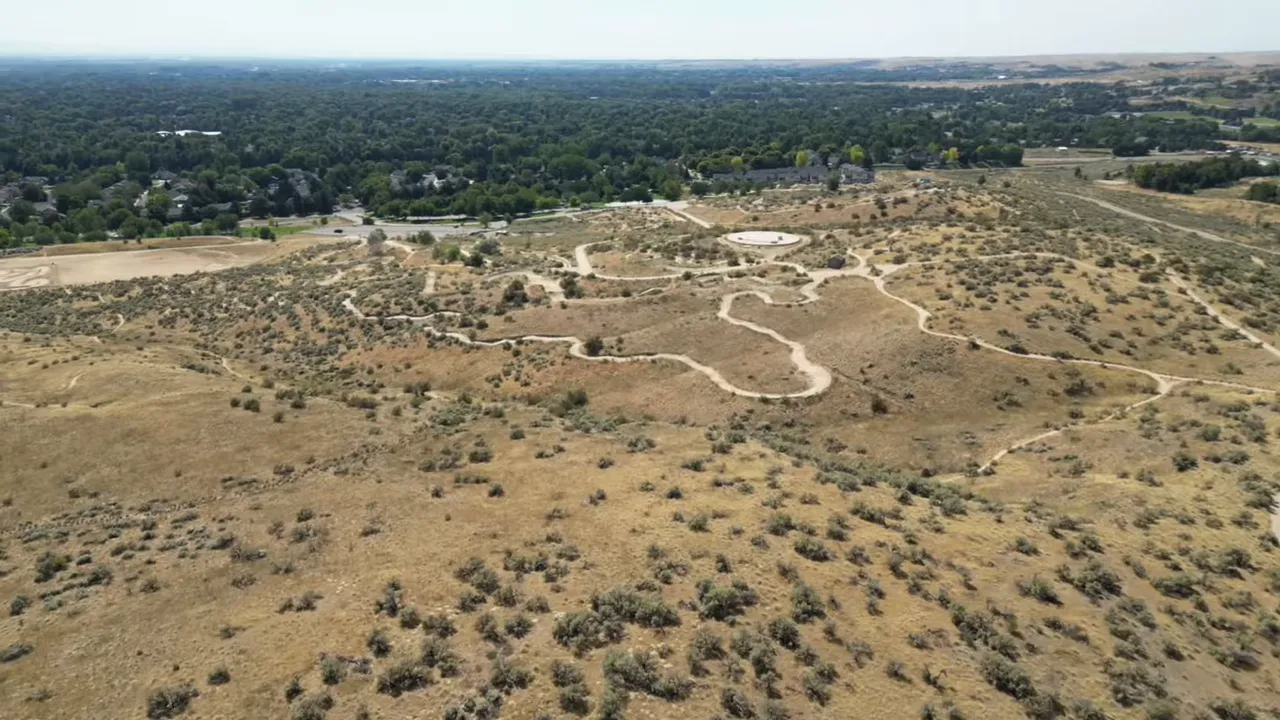 Aerial view of dry hillside landscape with trail paths and open area near Boise suburb