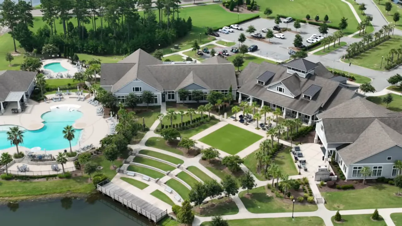high-resolution aerial view of the amenity center showing the main outdoor pool, clubhouse buildings, a grassy plaza, amphitheater seating and a dock on the lake